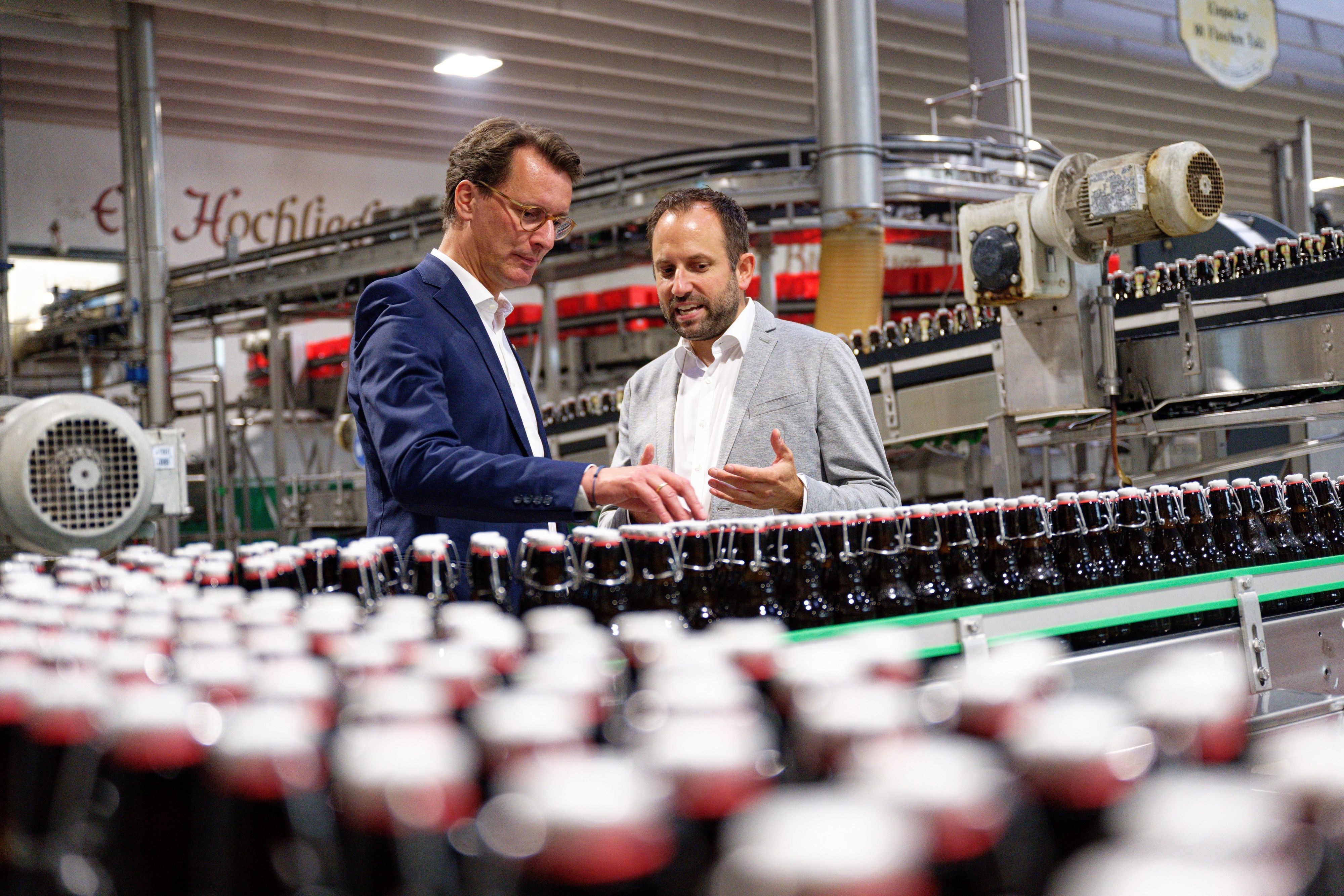 30.08.2023, Nordrhein-Westfalen, Oelde: Hendrik Wüst (CDU, l), Ministerpräsident von Nordrhein-Westfalen, steht bei einem Besuch von Pott·s Landbrauerei im Rahmen seiner Sommertour in einer Abfüllanlage neben dem Geschäftsführer Jörg Pott. Foto: Henning Kaiser/dpa +++ dpa-Bildfunk +++