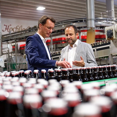 30.08.2023, Nordrhein-Westfalen, Oelde: Hendrik Wüst (CDU, l), Ministerpräsident von Nordrhein-Westfalen, steht bei einem Besuch von Pott·s Landbrauerei im Rahmen seiner Sommertour in einer Abfüllanlage neben dem Geschäftsführer Jörg Pott. Foto: Henning Kaiser/dpa +++ dpa-Bildfunk +++