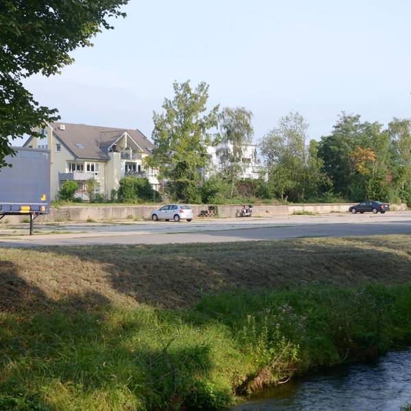 Auf einem Grundstück am Veybach in Euskirchen stehen mehrere Autos. Der größte Teil des Areals ist ungenutzt. Dort sollen Wohnhäuser entstehen.