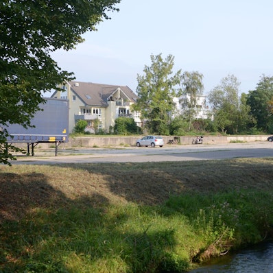 Auf einem Grundstück am Veybach in Euskirchen stehen mehrere Autos. Der größte Teil des Areals ist ungenutzt. Dort sollen Wohnhäuser entstehen.