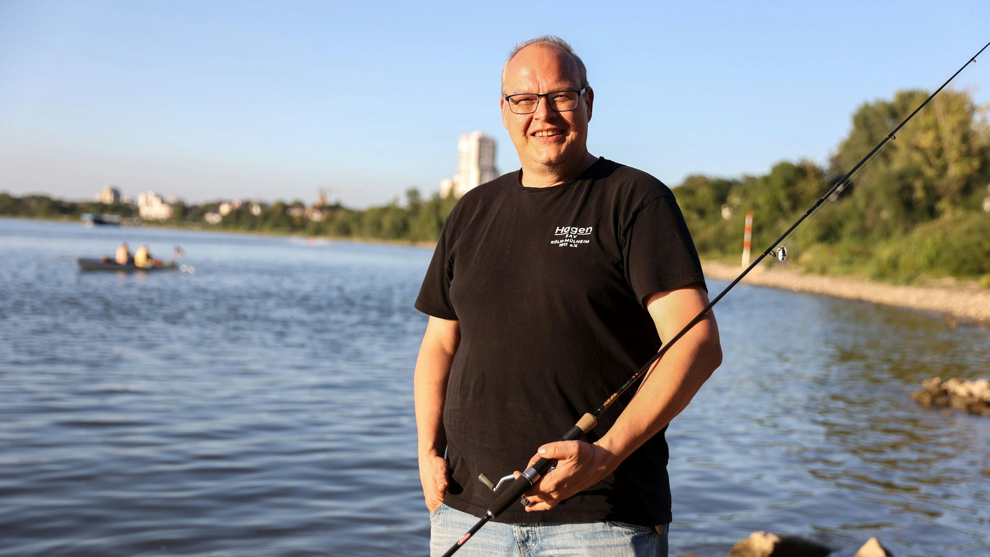 Hagen Hoffmann vom Sportanglerverein Mülheim steht in Porz mit seiner Angel in der Hand am Rhein.