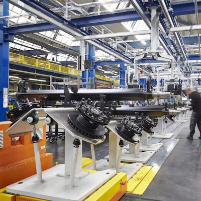 Man sieht Bestandteile einer LKW-Achse und einen Arbeiter in einer großen Fabrikhalle.