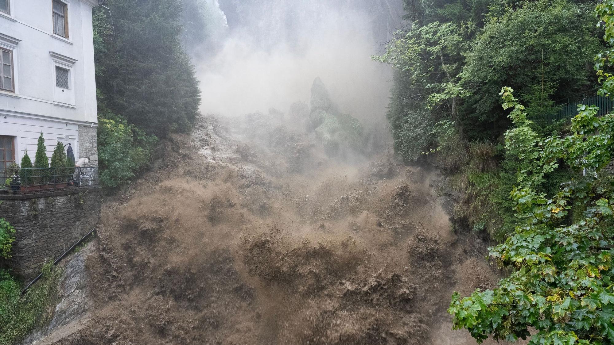 Ein durch Regenmassen und Schlamm verursachter Sturzbach am Wasserfall Gasteinfall im österreichischen Bad Gastein. Die Wassermassen sind kurz davor, eine Brücke zu überschwemmen.