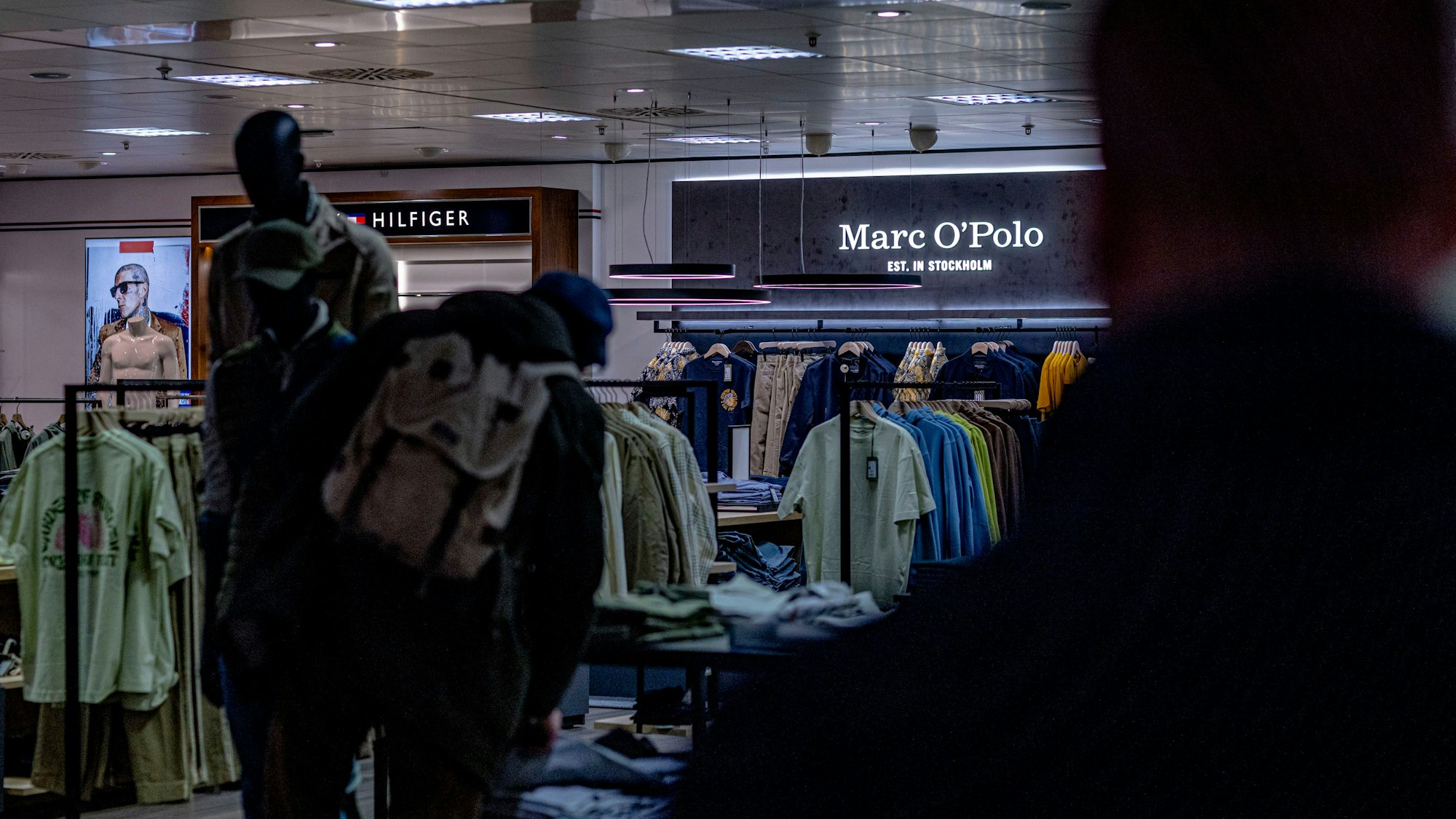 Man sieht das Innere eines Ladens, in dem eine Person mit einem Rucksack die Ware begutachtet.