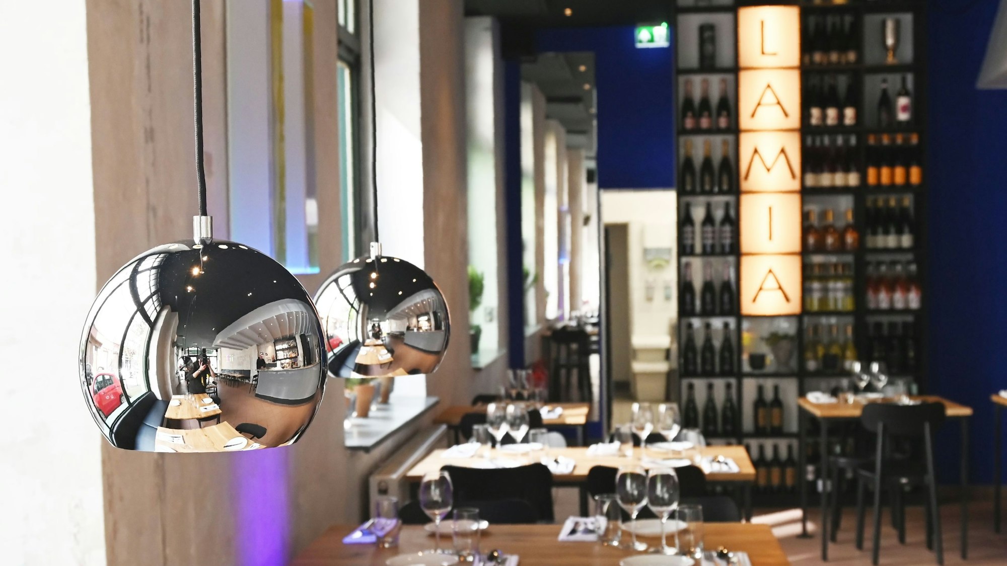 Stilvolle Inneneinrichtung des Restaurants mit silbernen Lampen und Weinregal.