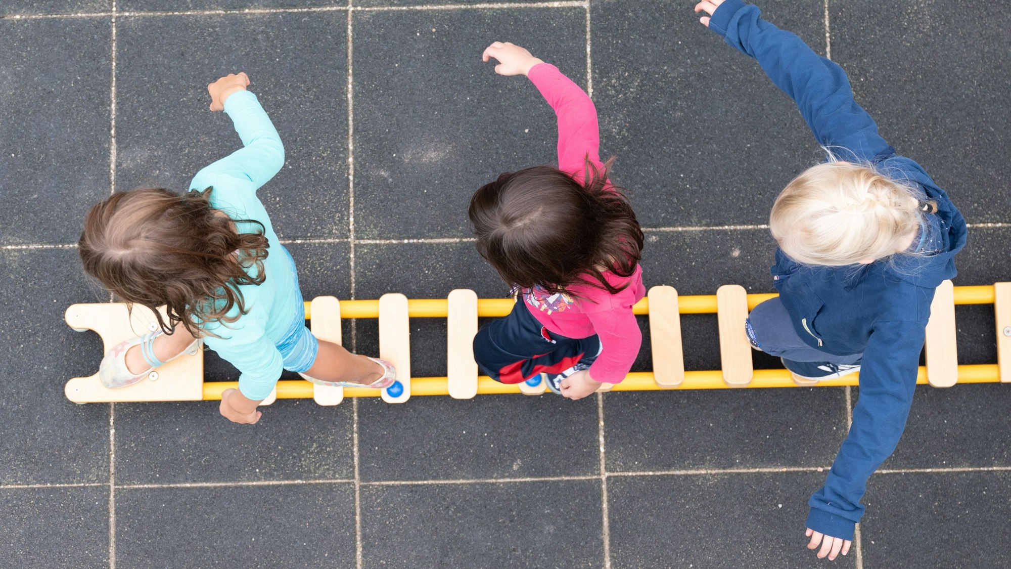 Kinder balancieren auf dem Spielplatz einer Kindertagesstätte auf einem Brett.