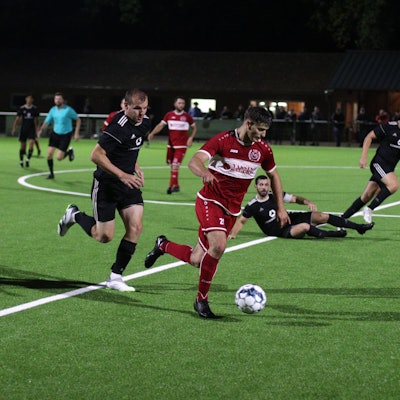 Ein Fußballspieler führt einen Ball und wird vom Gegner verfolgt.