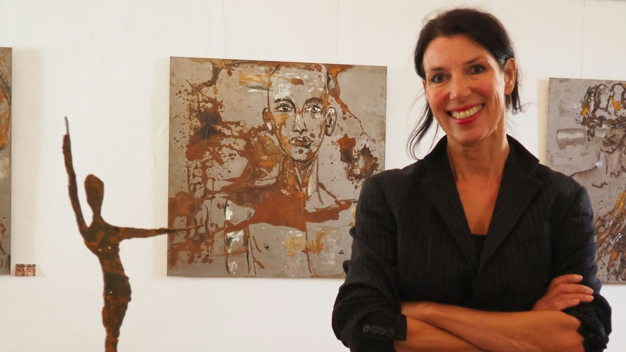 Eine Frau steht vor einem Bild, daneben ist eine Figur aus Metall platziert.