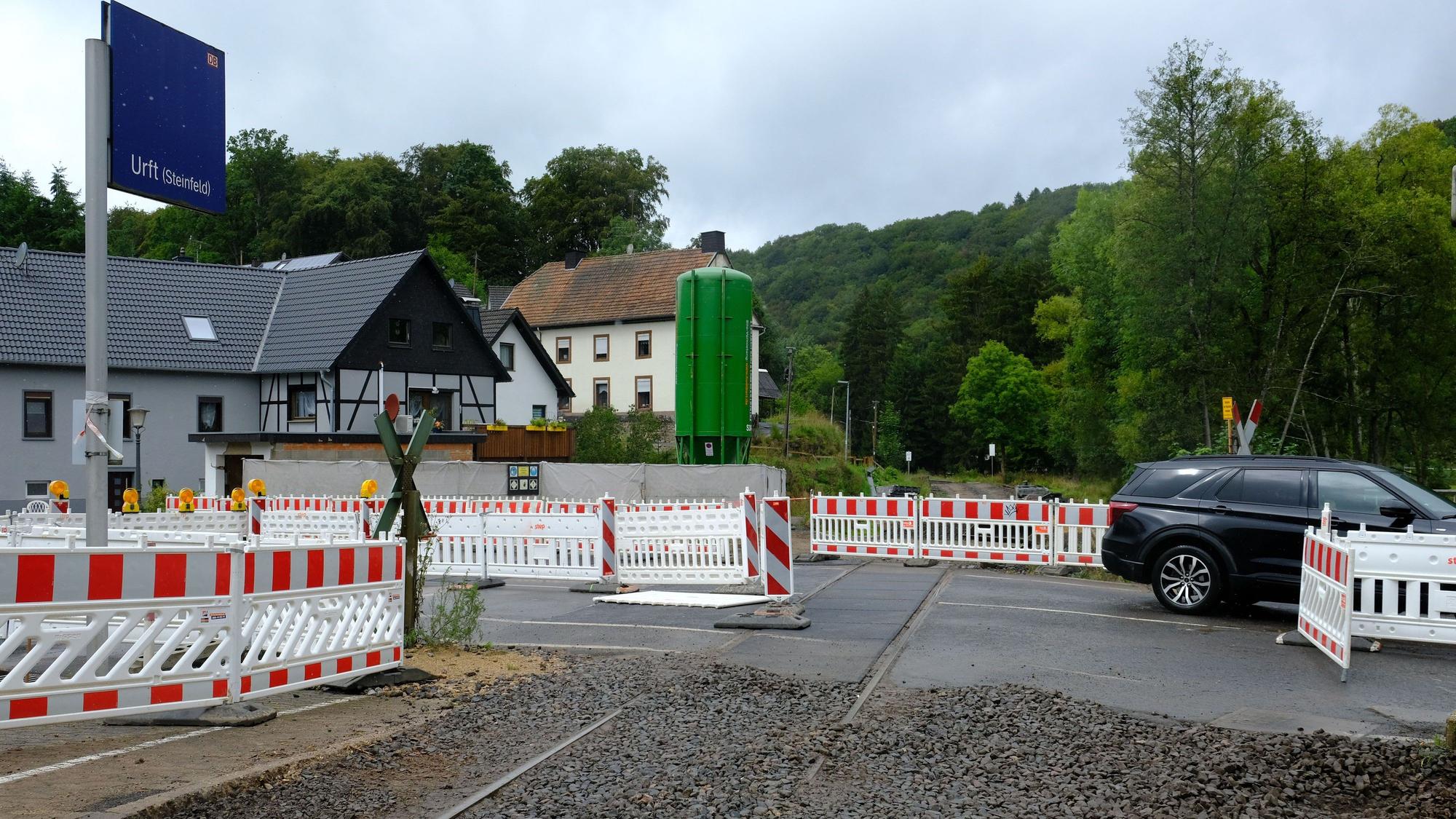 An der Baustelle des Bahnübergangs in Urft stehen Absperrungen, ein Auto fährt vorüber.