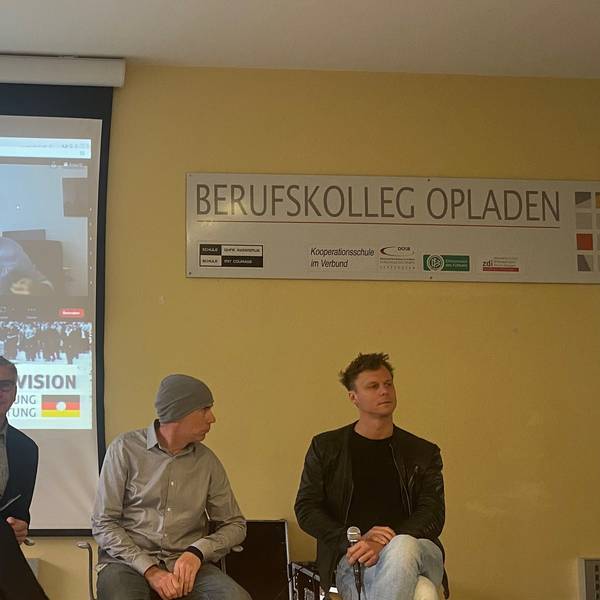 Podiumsdiskussion zu Aufständen und Protesten am Berufskolleg Opladen: Dr. Günter Hinken (v.l.), Tim Eisenlohr, Alex Wernke, auf der Leinwand: Ehsan Ayatollahi.