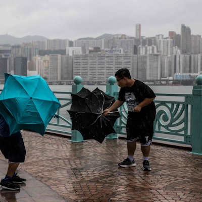 TOPSHOT - People struggle with their umbrellas in high winds brought by Super Typhoon Saola next to Victoria harbour in Hong Kong on September 1, 2023. Super Typhoon Saola threatened southern China on September 1 with some of the strongest winds the region has endured, forcing the megacities of Hong Kong and Shenzhen to effectively shut down. (Photo by ISAAC LAWRENCE / AFP)