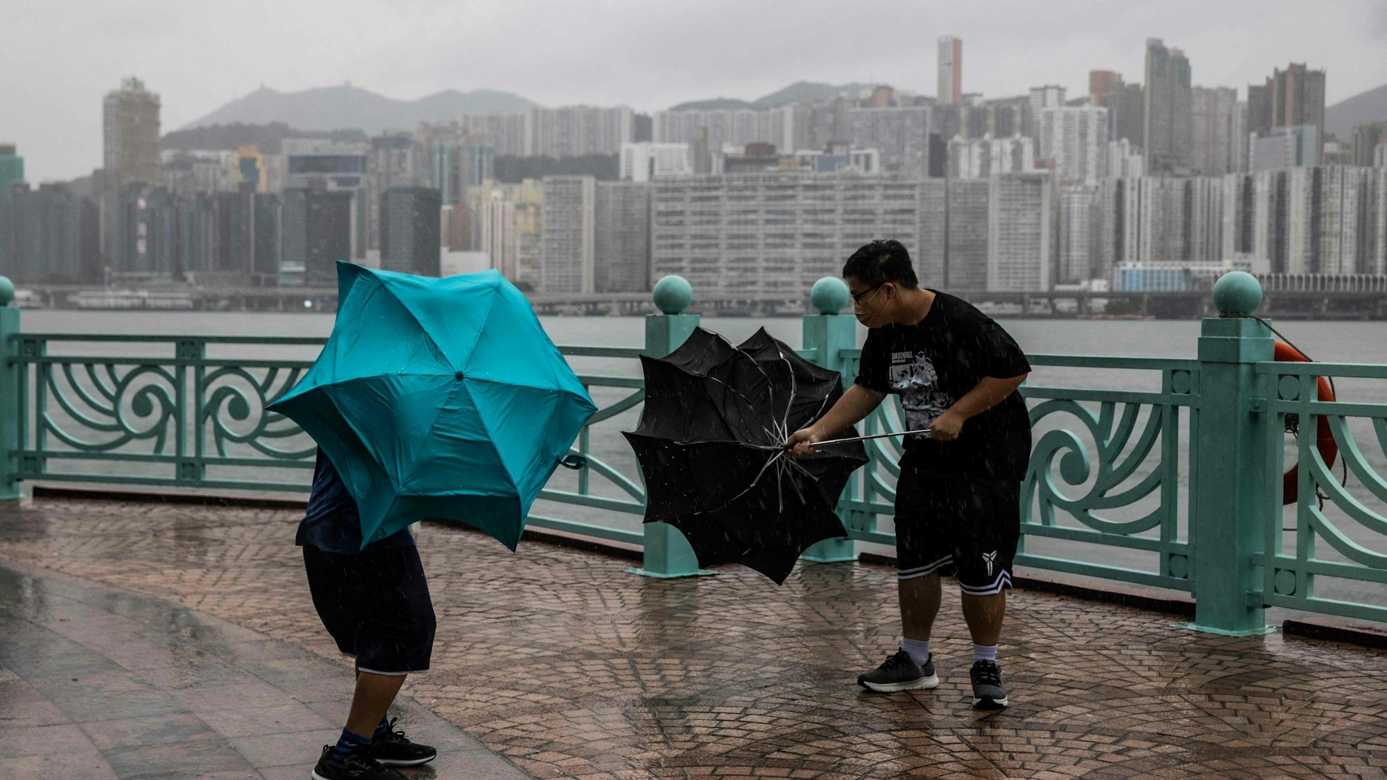 TOPSHOT - People struggle with their umbrellas in high winds brought by Super Typhoon Saola next to Victoria harbour in Hong Kong on September 1, 2023. Super Typhoon Saola threatened southern China on September 1 with some of the strongest winds the region has endured, forcing the megacities of Hong Kong and Shenzhen to effectively shut down. (Photo by ISAAC LAWRENCE / AFP)