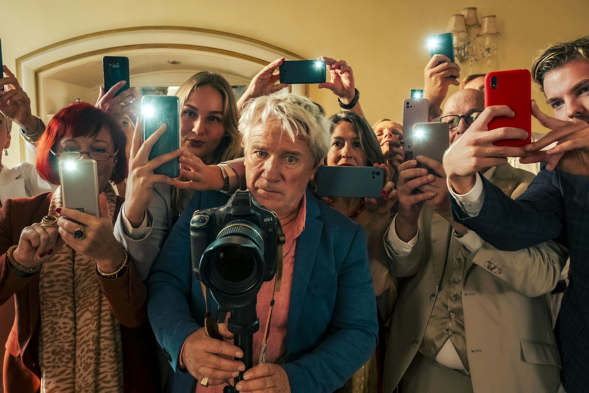 Der Schauspieler Jörg Schüttauf steht mit einer digitalen Spiegelreflexkamera umringt von Menschen, die mit ihren Smartphones fotografieren.