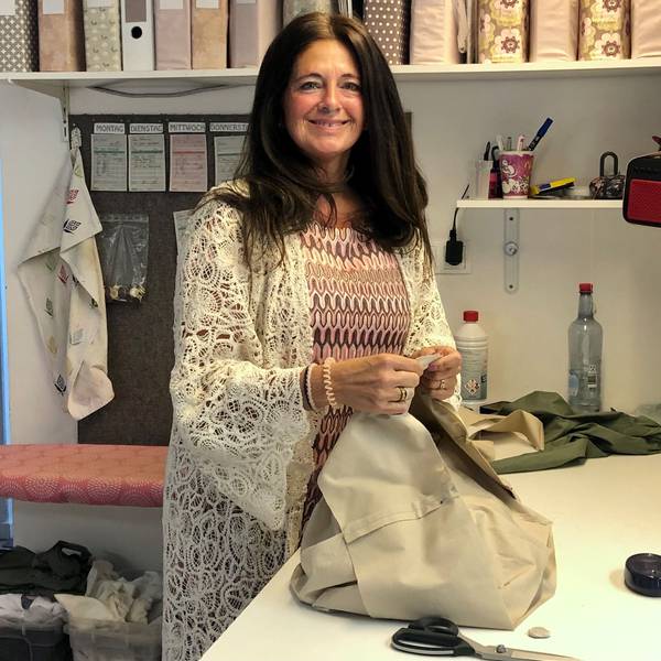 Eine Frau mit langen braunen Haare steht lächelnd an einem Schneidertisch.