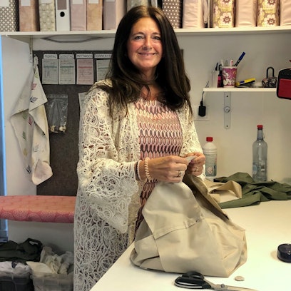 Eine Frau mit langen braunen Haare steht lächelnd an einem Schneidertisch.
