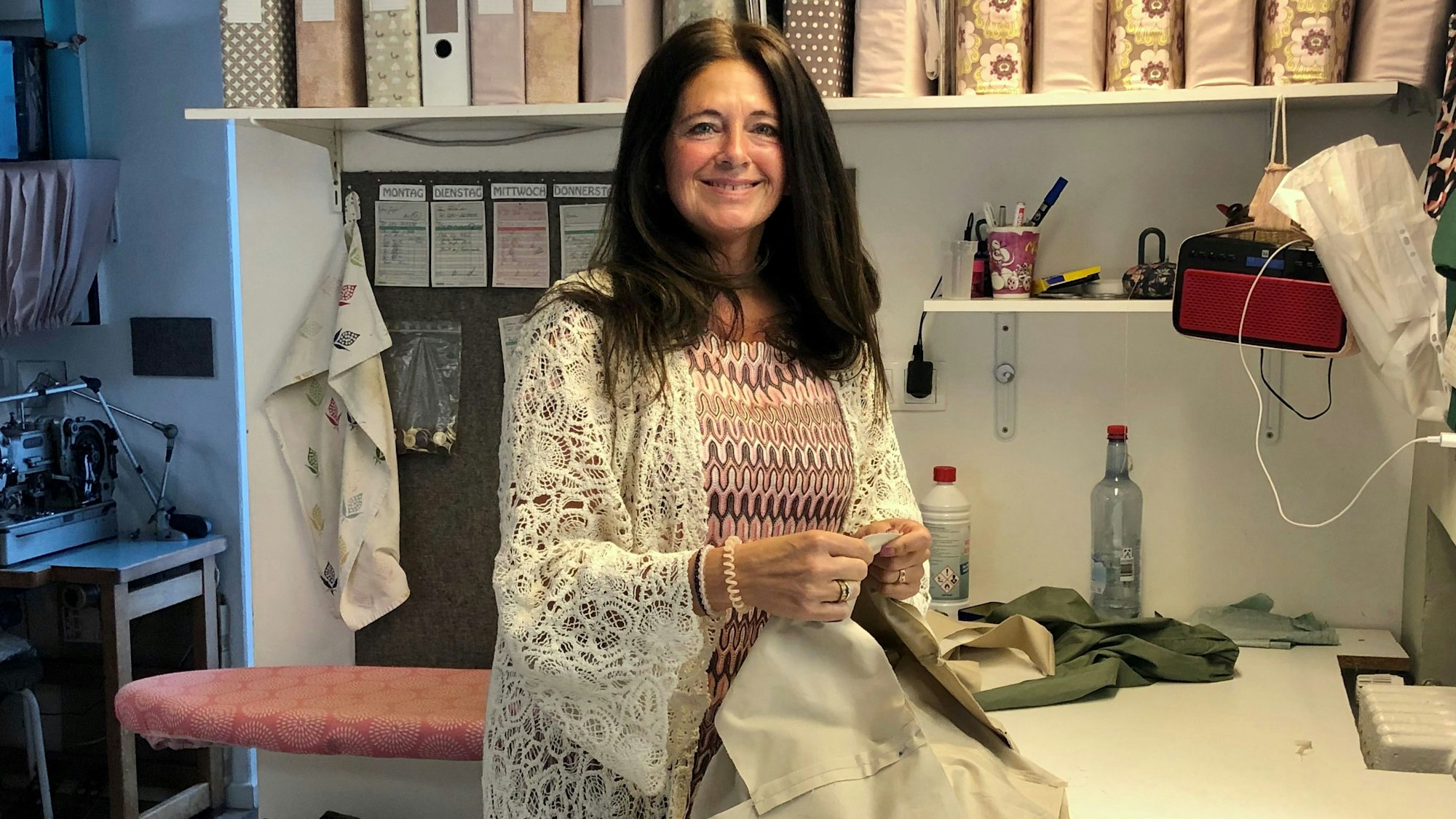 Eine Frau mit langen braunen Haare steht lächelnd an einem Schneidertisch.
