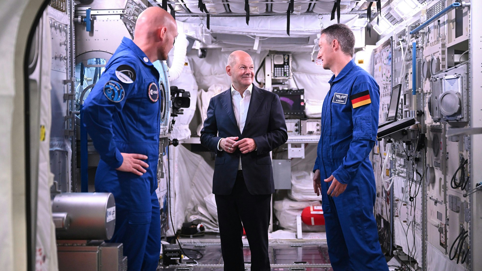 Bundeskanzler Olaf Scholz (SPD, M) steht mit den deutschen ESA-Astronauten Matthias Maurer (r) und Alexander Gerst in einem Modell des Columbus-Moduls in der Neutral Bouyancy Facility, während eines Besuchs im Astronautenzentrum der Europäischen Weltraumorganisation ESA.