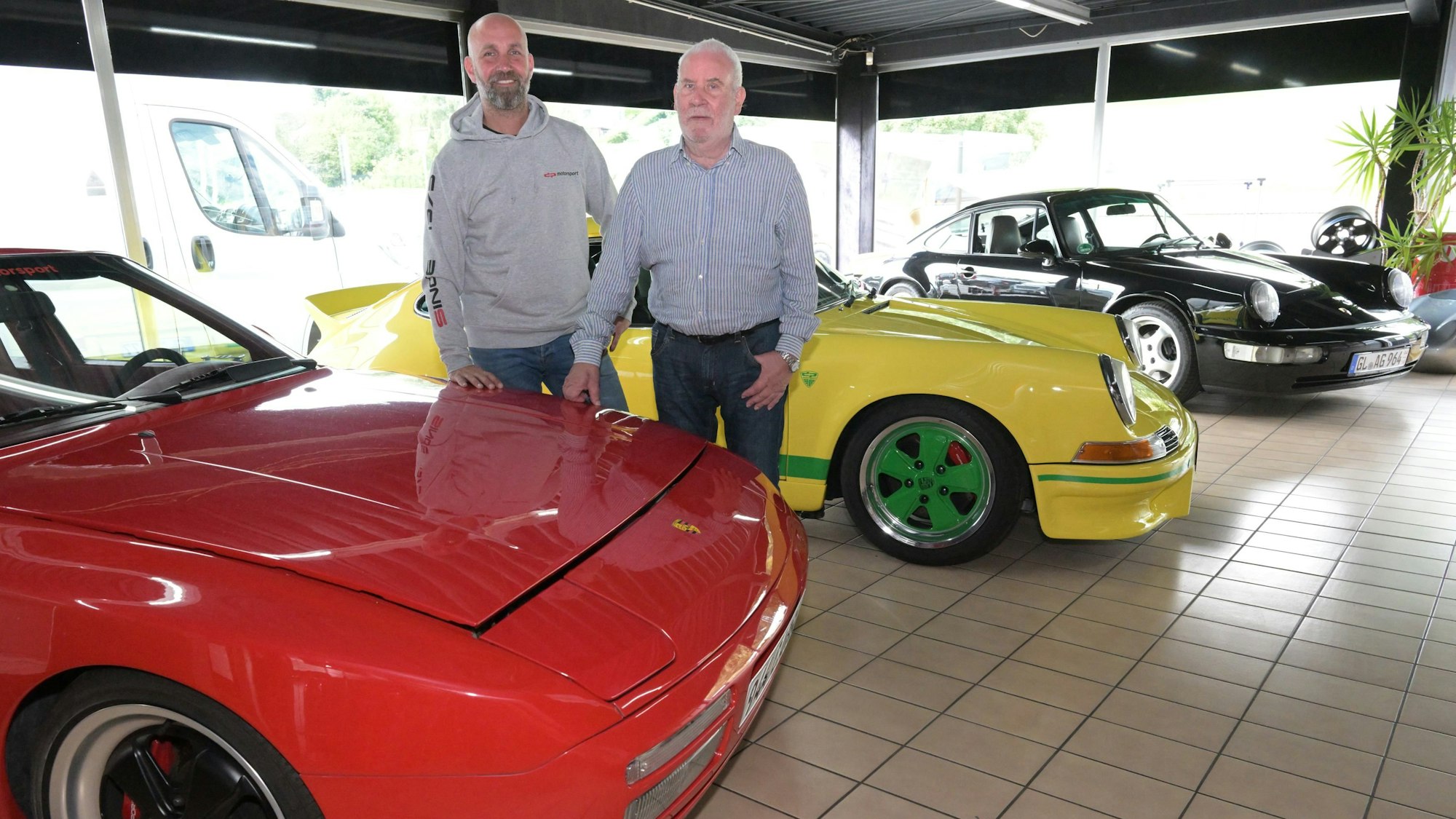 Zwei Männer stehen zwischen porsche-Fahrzeugen in einer Halle.
