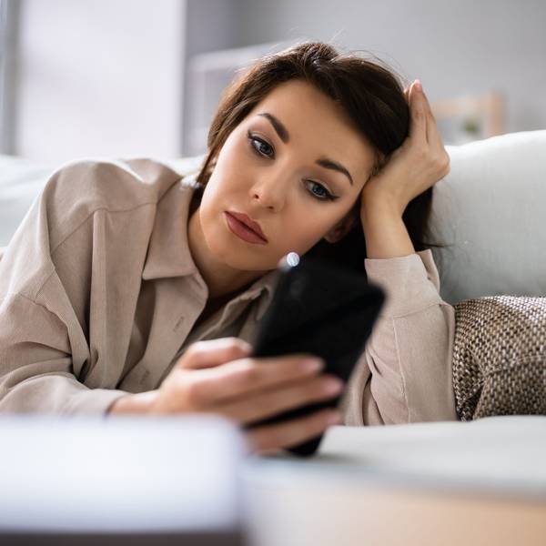 Eine Frau liegt auf der Couch und wartet auf eine Nachricht von der Person, die sie datet.