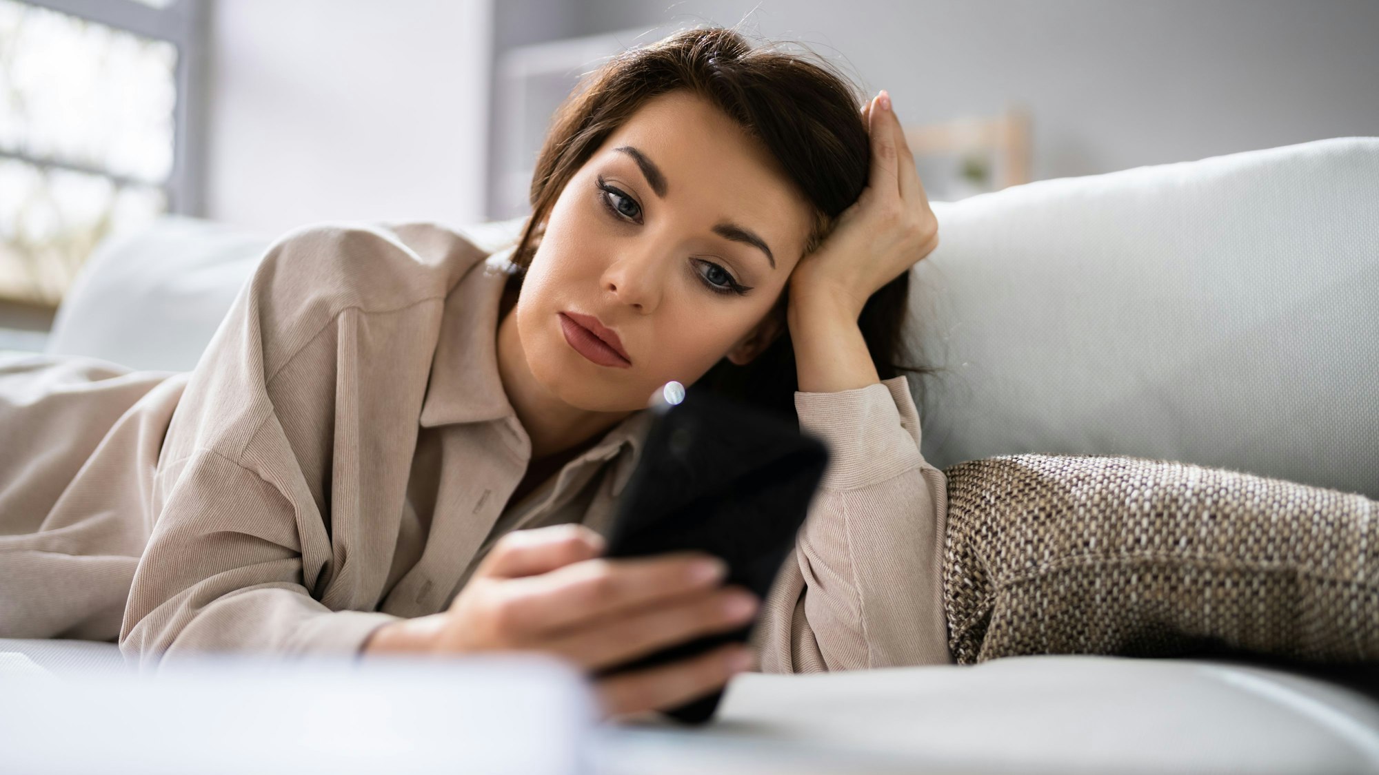 Eine Frau liegt auf der Couch und wartet auf eine Nachricht von der Person, die sie datet.