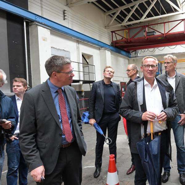 Eine Frau steht mit vielen Männern in einer Halle der ehemaligen Papierfabrik Zanders in Bergisch Gladbach.