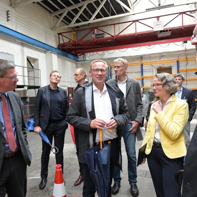 Eine Frau steht mit vielen Männern in einer Halle der ehemaligen Papierfabrik Zanders in Bergisch Gladbach.