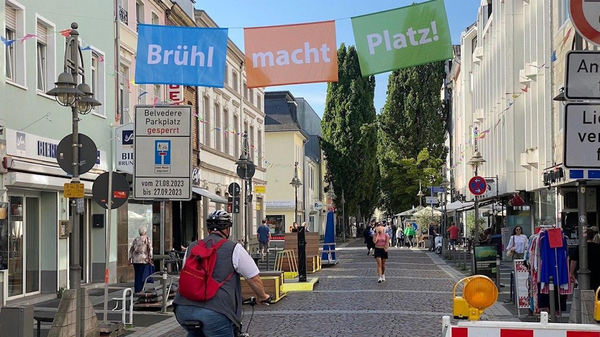 Das Bild zeigt die Kölnstraße, die von einem Banner mit der Aufschrift „Brühl macht Platz“ überspannt ist.