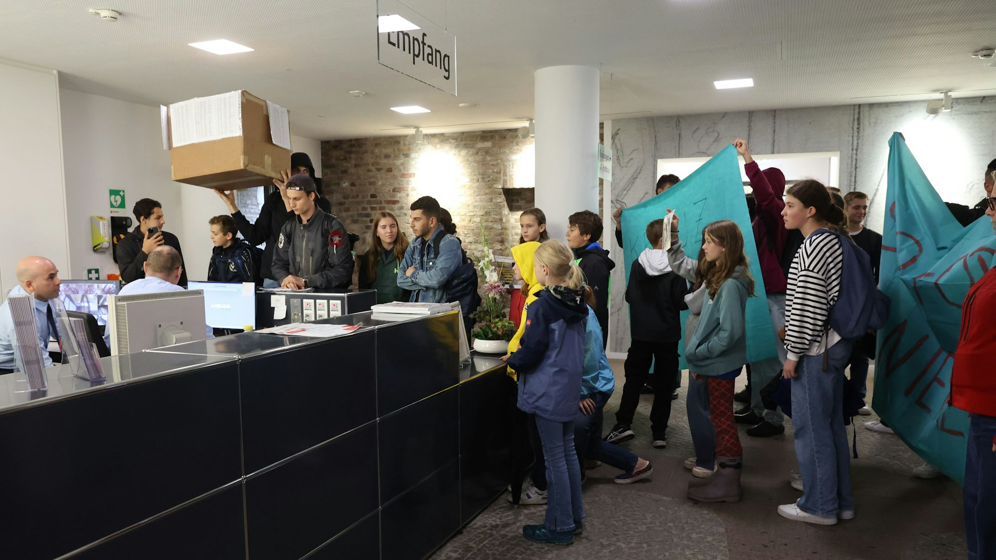 Eine Gruppe von Schülerinnen und Schülern steht im Foyer des Historischen Rathauses. Einige halten Transparente, ein Schüler hält einen großen Karton in den Händen.