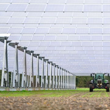 Blick auf eine große Photovoltaikanlage, unter der ein Traktor hindurchfährt.