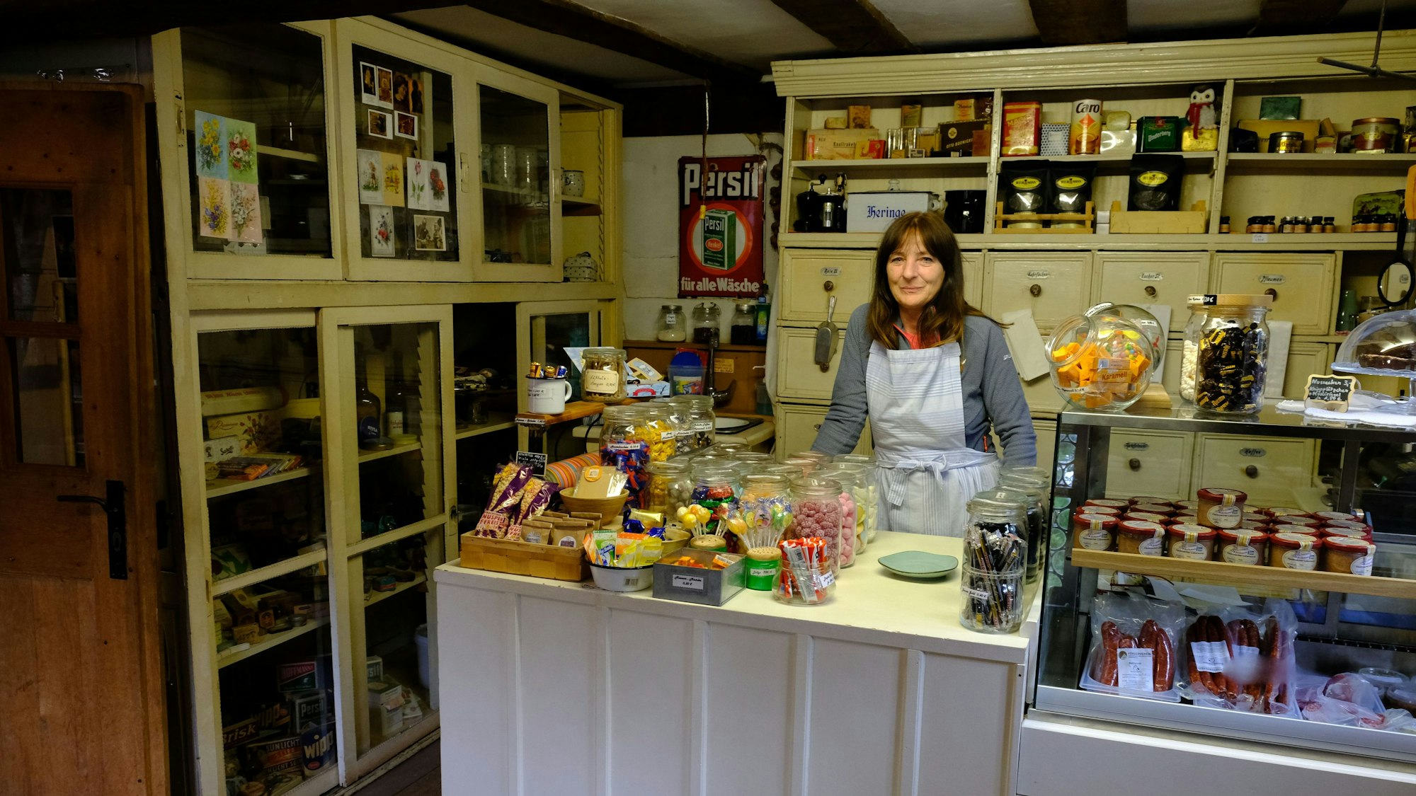 Im Freilichtmuseum Kommern steht eine Mitarbeiterin an der Verkaufstheke eines historischen Tante-Emma-Ladens.