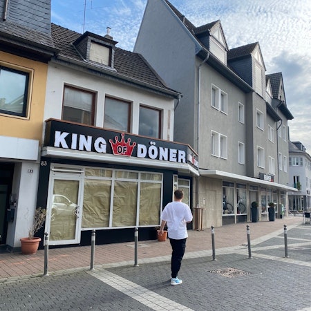 Das Bild zeigt eine Außenansicht des neuen Restaurants. Noch sind die Scheiben abgeklebt. Über der Tür steht die große Leuchtreklame mit dem Schriftzug King of Döner.