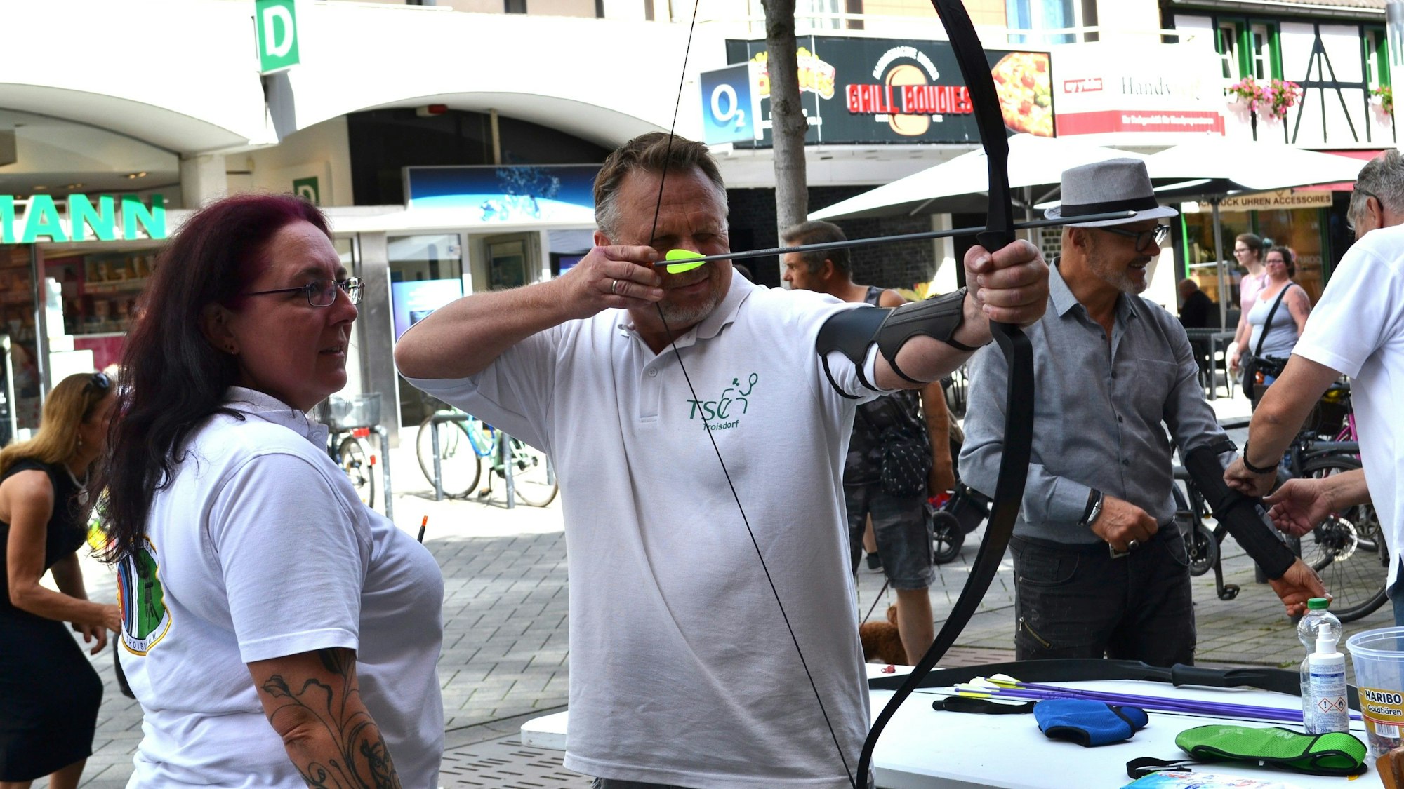 Ein Mann im weißen Vereins-T-Shirt spannt den Bogen mit einem Pfeil.