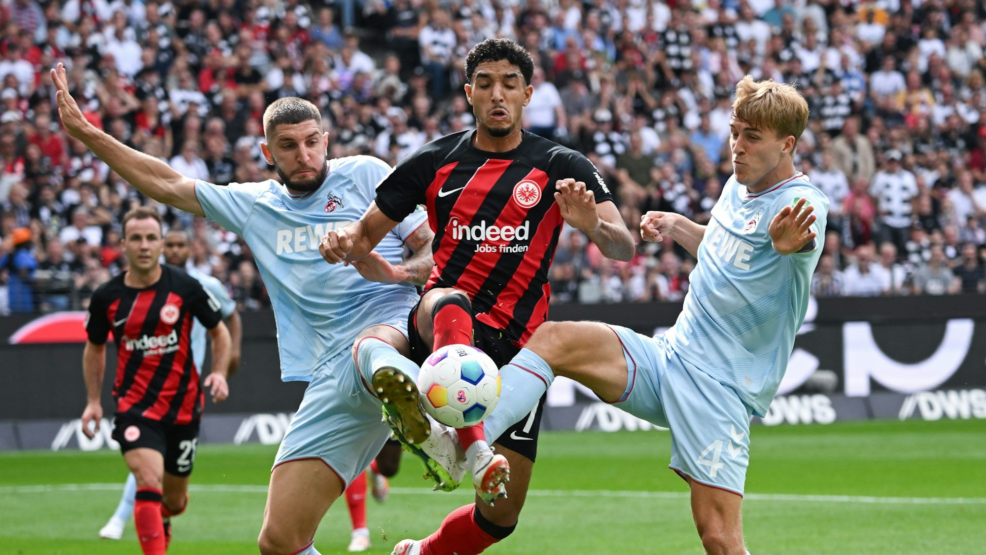 Frankfurts Omar Marmoush (M) und die Kölner Jeff Chabot (l) und Timo Hübers kämpfen um den Ball.