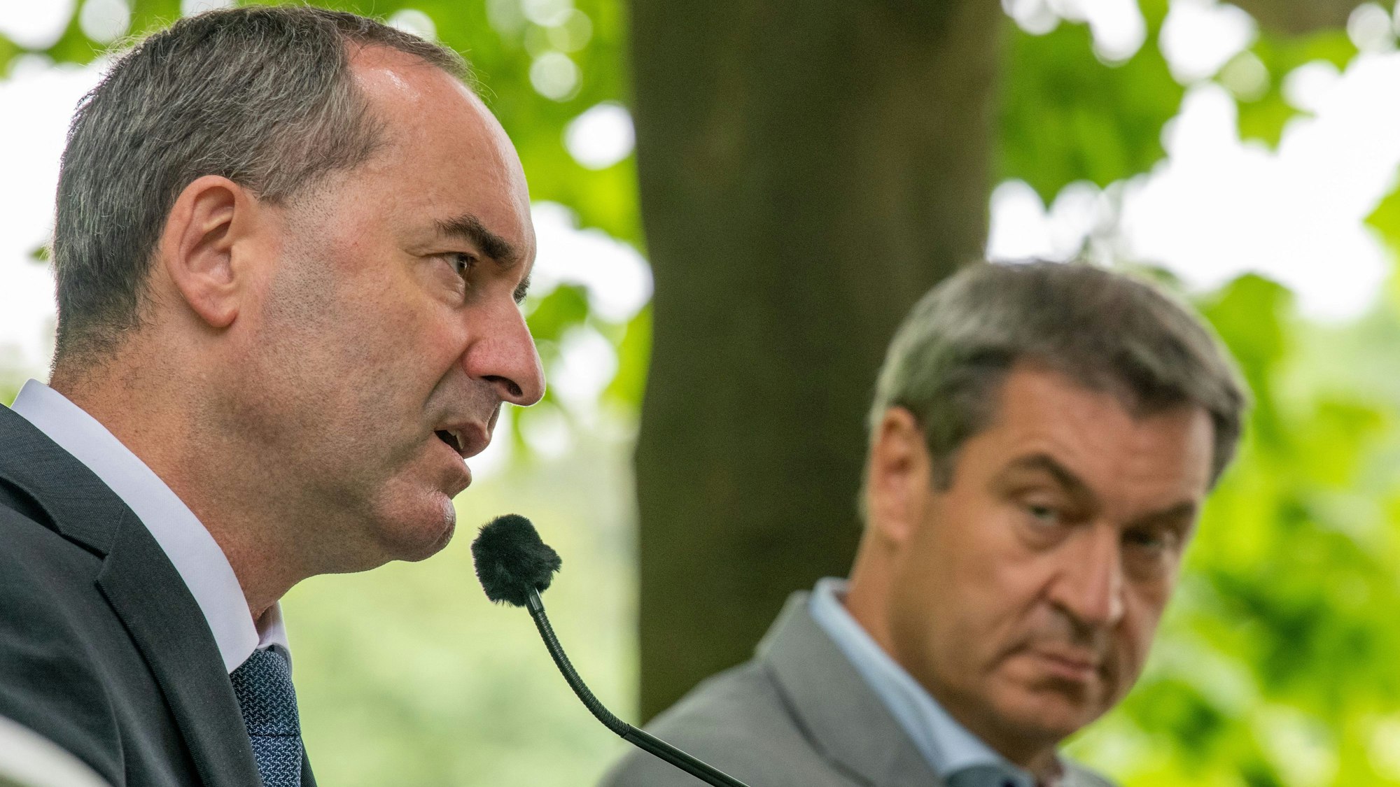 Hubert Aiwanger (Freie Wähler) spricht in ein Mikrofon, während ihm Markus Söder (CSU) dabei zusieht.