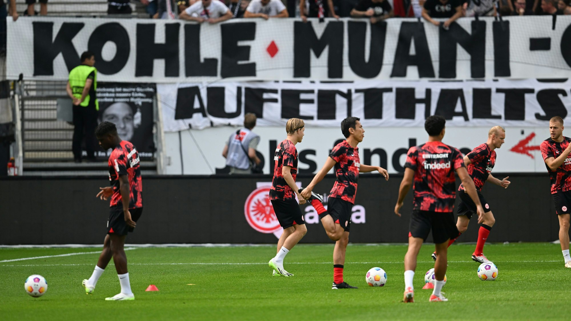 Frankfurts Spieler bereiten sich vor. Dahinter nehmen die Eintracht-Fans den Abgang von Kolo Muani mit Humor.