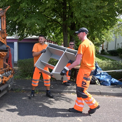 Zwei Männer werfen Sperrmüll in ein Müllfahrzeug.