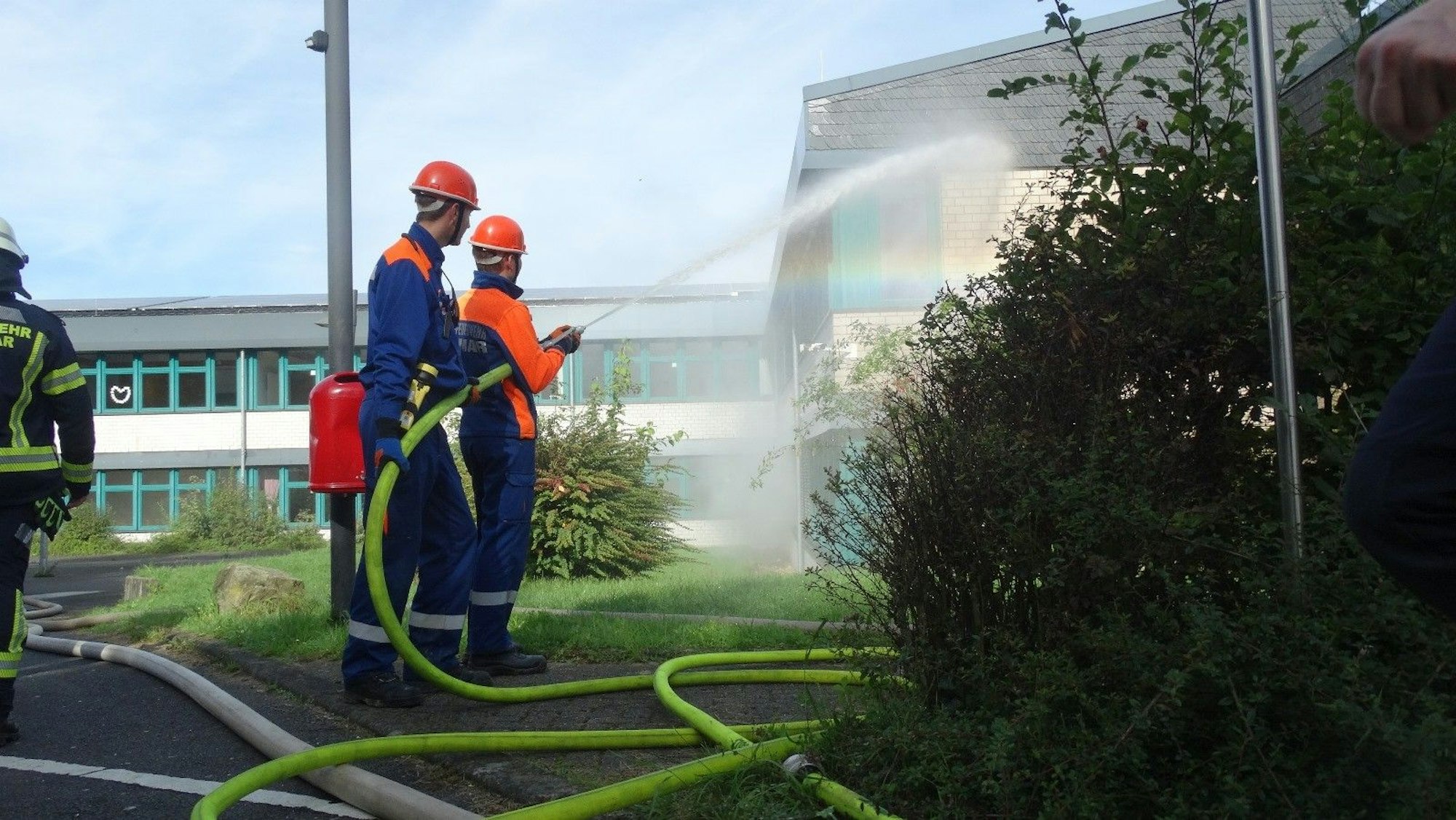 Zwei Jugendliche in den Uniformen der Jugendfeuerwehr halten einen dicken, gelben Schlauch und spritzen Löschwasser auf ein Gebäude.
