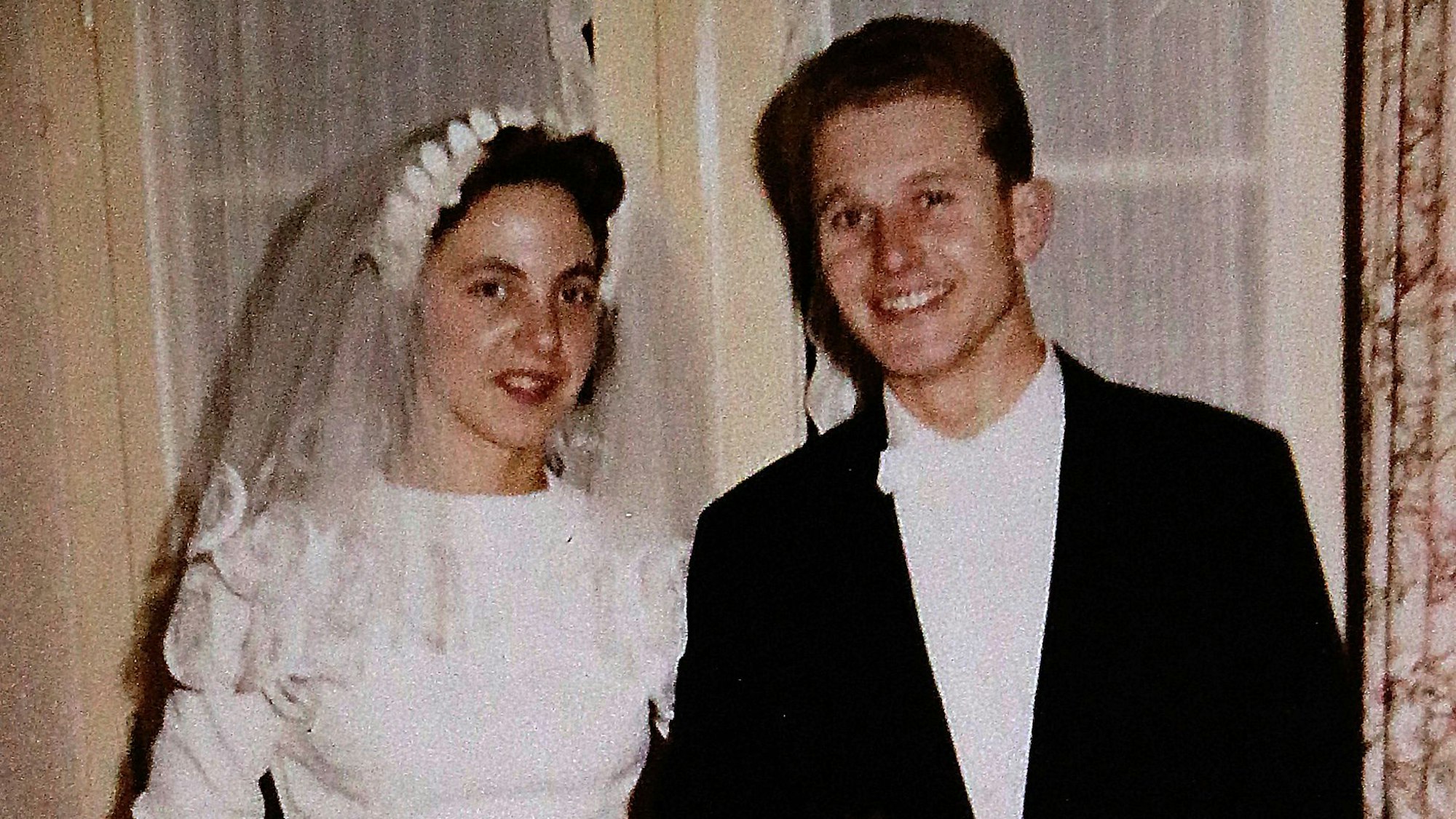 Eine Braut im weißen Kleid und mit Schleier neben einem Bräutigam mit schwarzem Jackett, weißem Hemd und weißer Fliege.