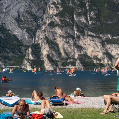 Urlauber liegen und stehen an einem Strand am italienischen Gardasee.