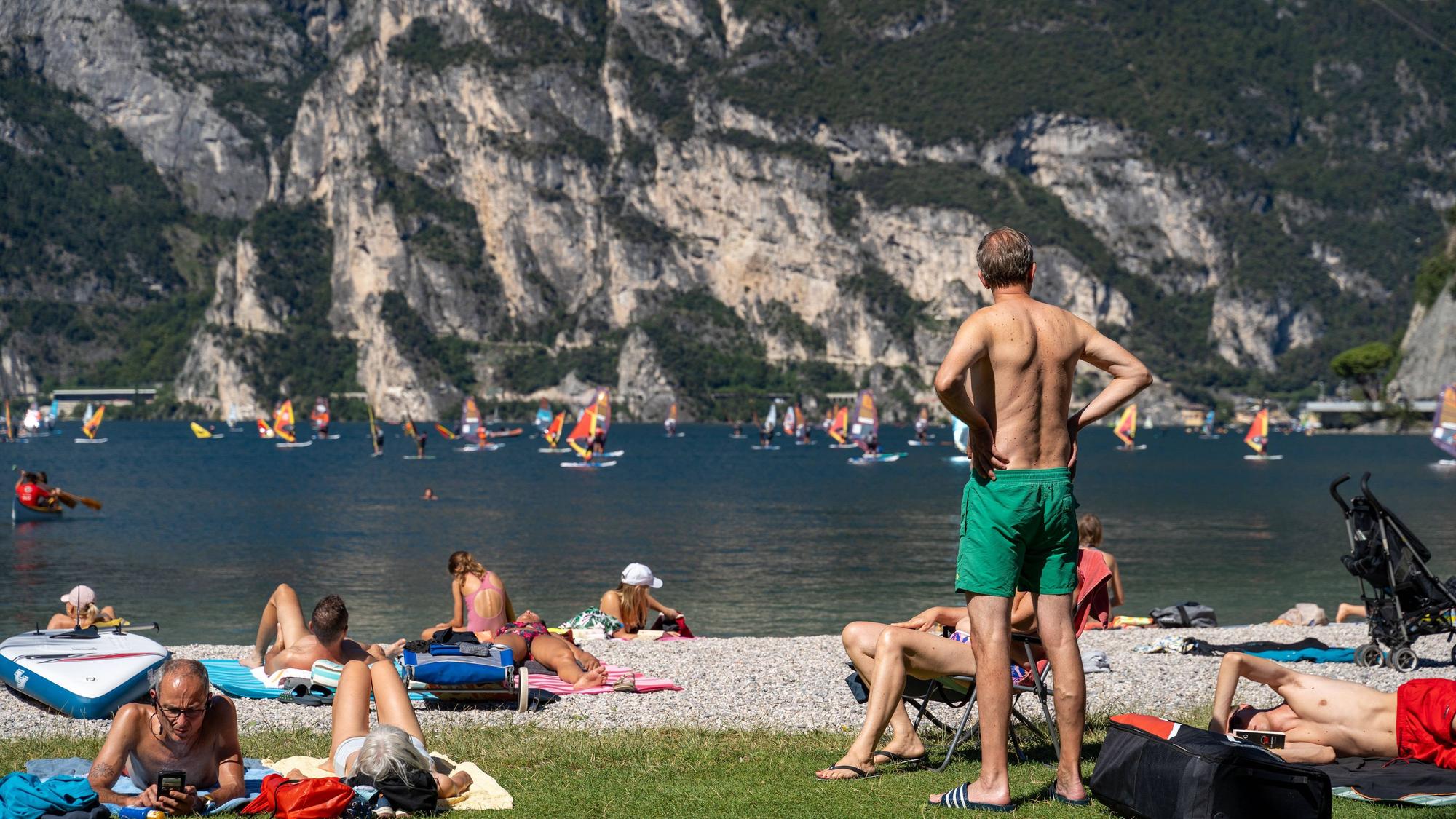 Urlauber liegen und stehen an einem Strand am italienischen Gardasee.