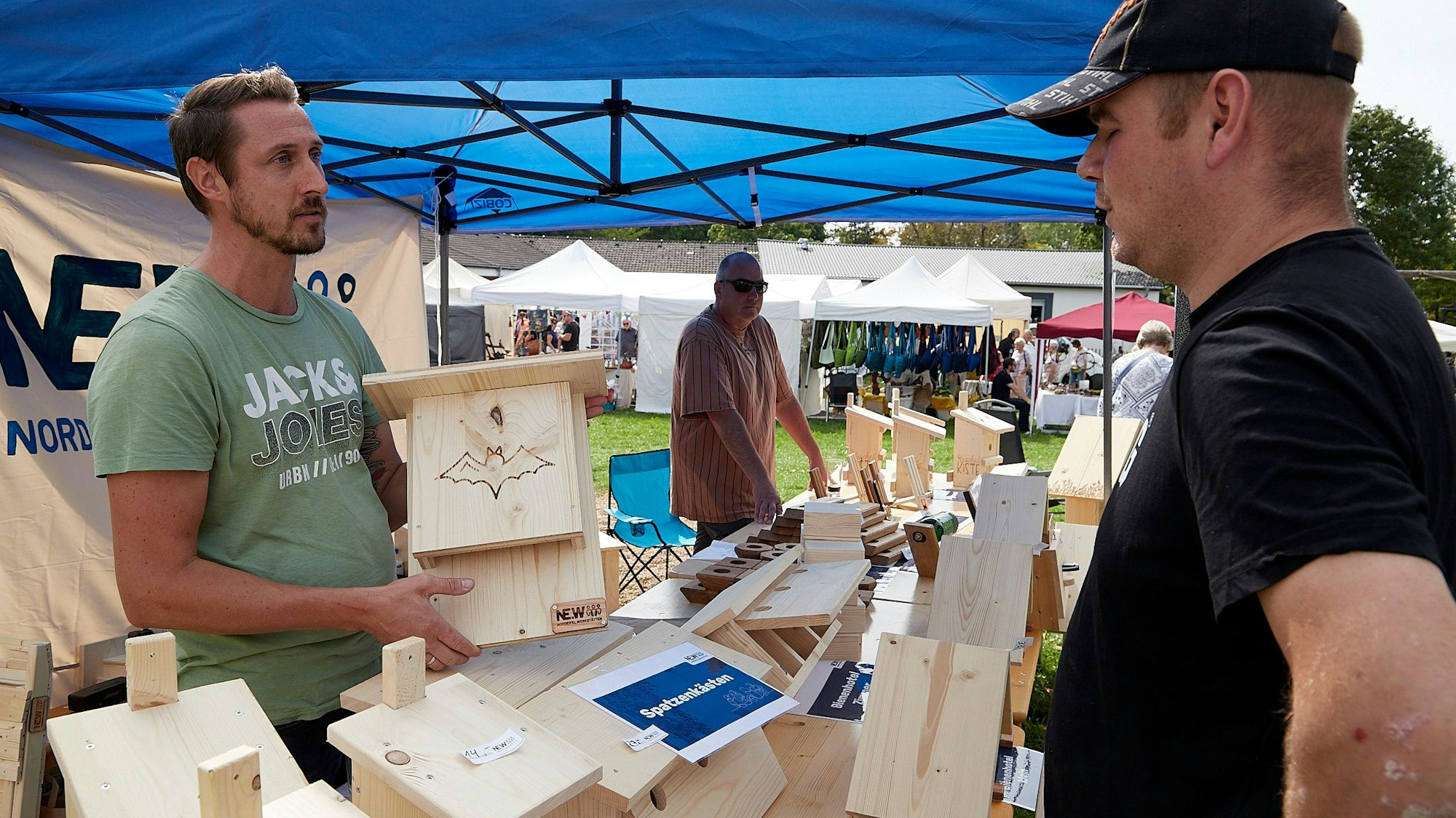 Ein Mann hält eine hölzerne Fledermaushöhle in der Hand und spricht mit einem anderen Mann.