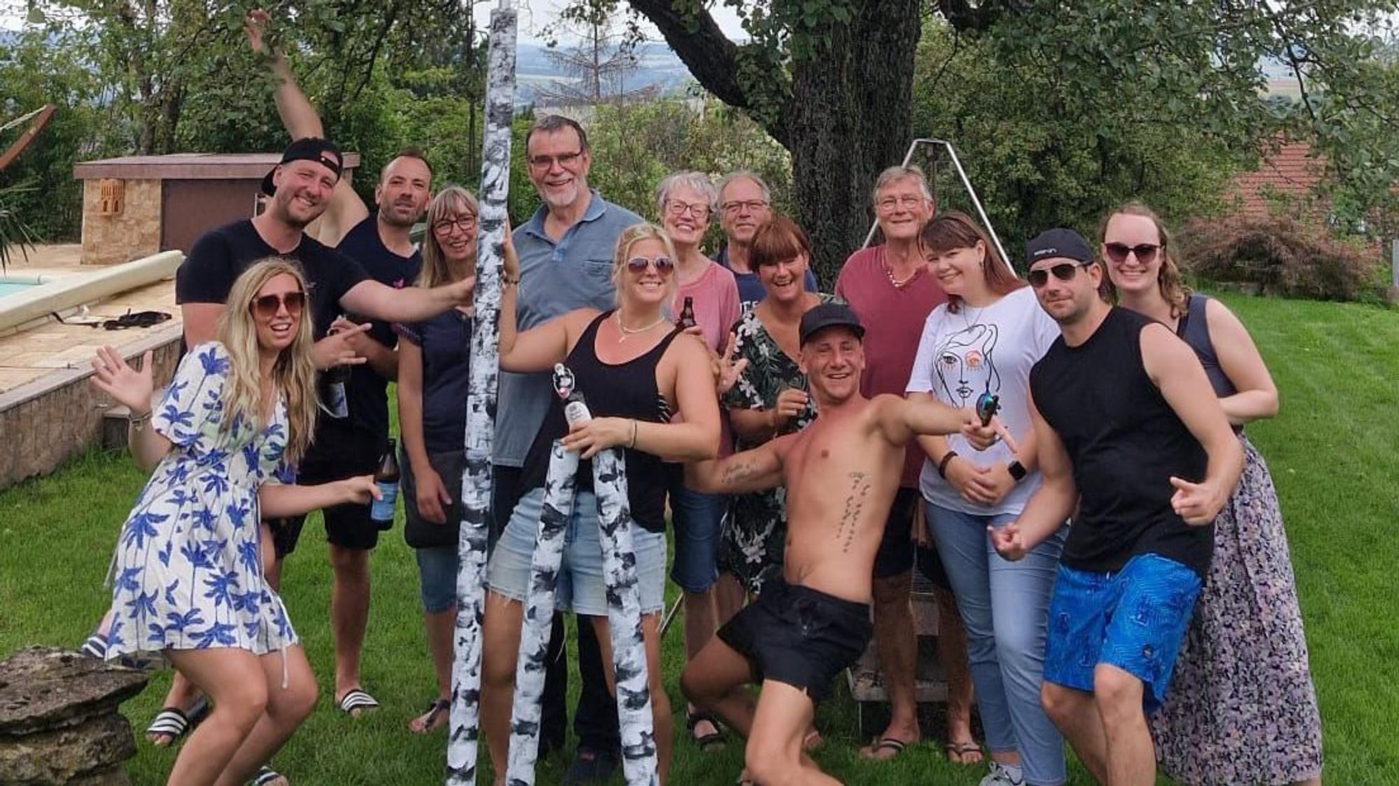 Eine Gruppe Menschen posiert gut gelaunt mit einer als Birke angemalten Teleskop-Stange.