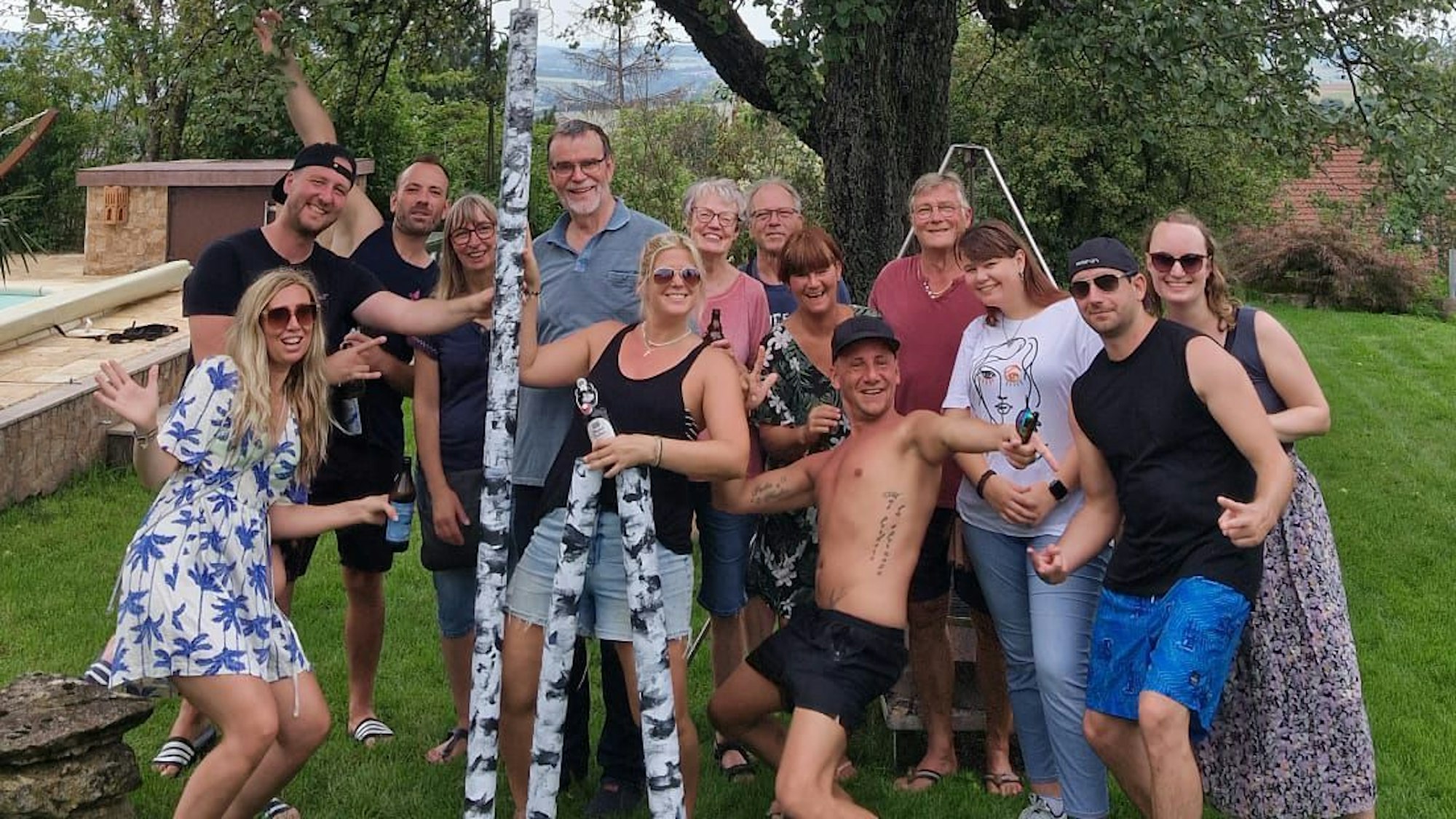 Eine Gruppe Menschen posiert gut gelaunt mit einer als Birke angemalten Teleskop-Stange.