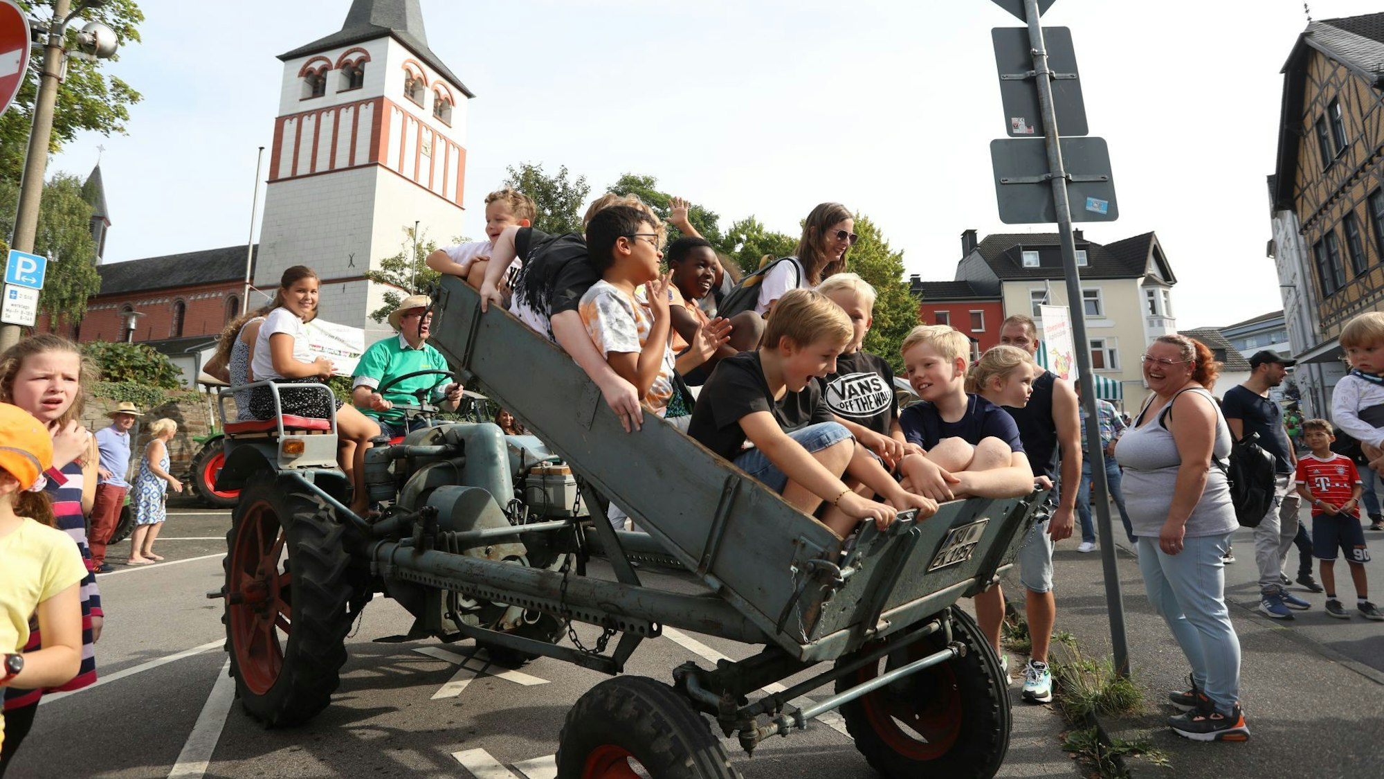 Lachende Kinder sitzen in einem Kipphänger vor einem Traktor, der soeben aufgestellt wird.
