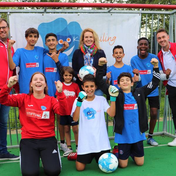 Junge Fußballer von dem Kölner Verein „Kidsmiling“ und Vereinsmitarbeiterinnen und -Mitarbeiter stehen vor einem Tor in Siegerposen.