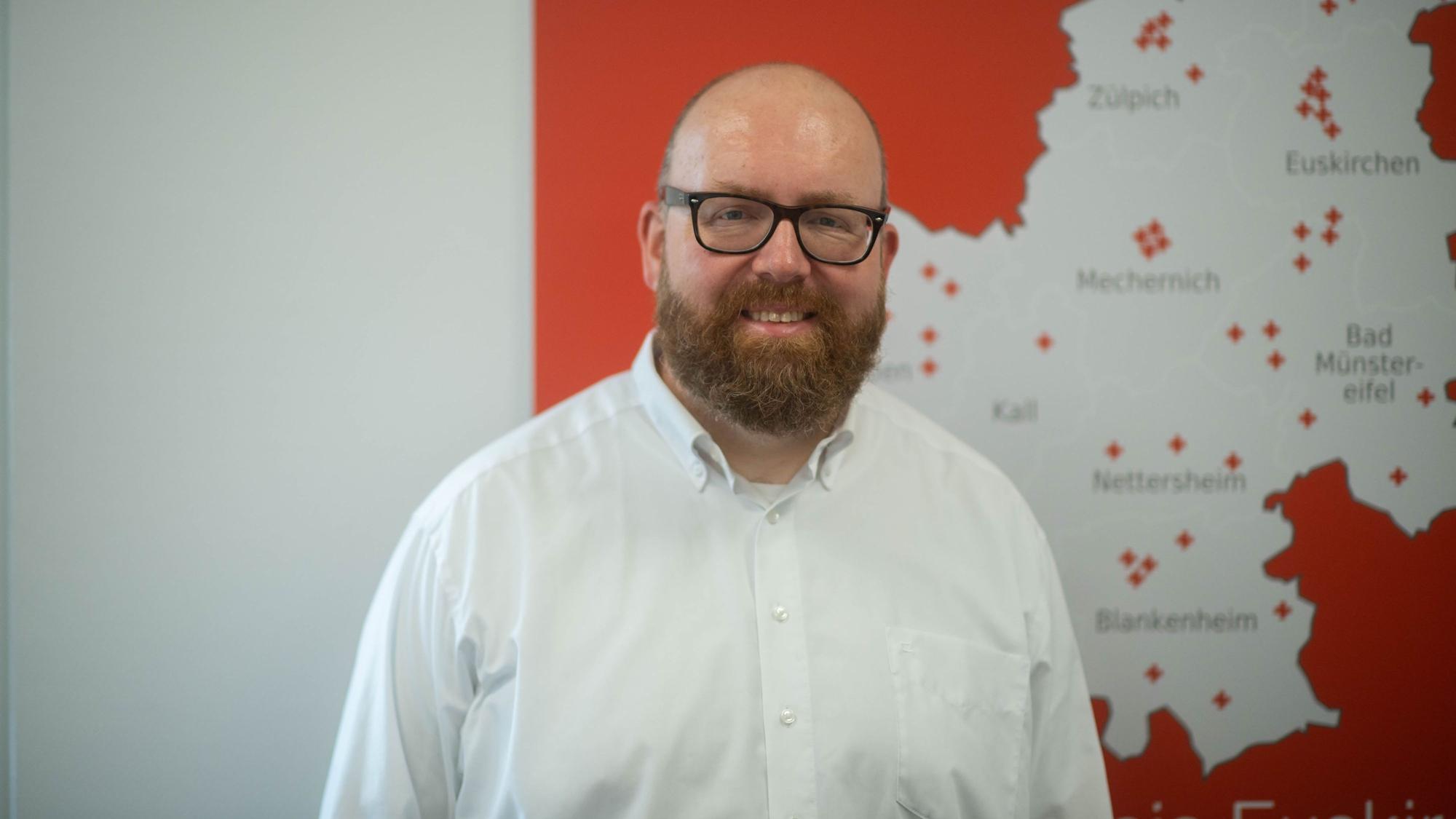 Boris Brandhoff ist Chef der Integrationsagentur des Deutschen Roten Kreuzes im Kreis Euskirchen. Er steht vor einer Karte des Kreises Euskirchen.
