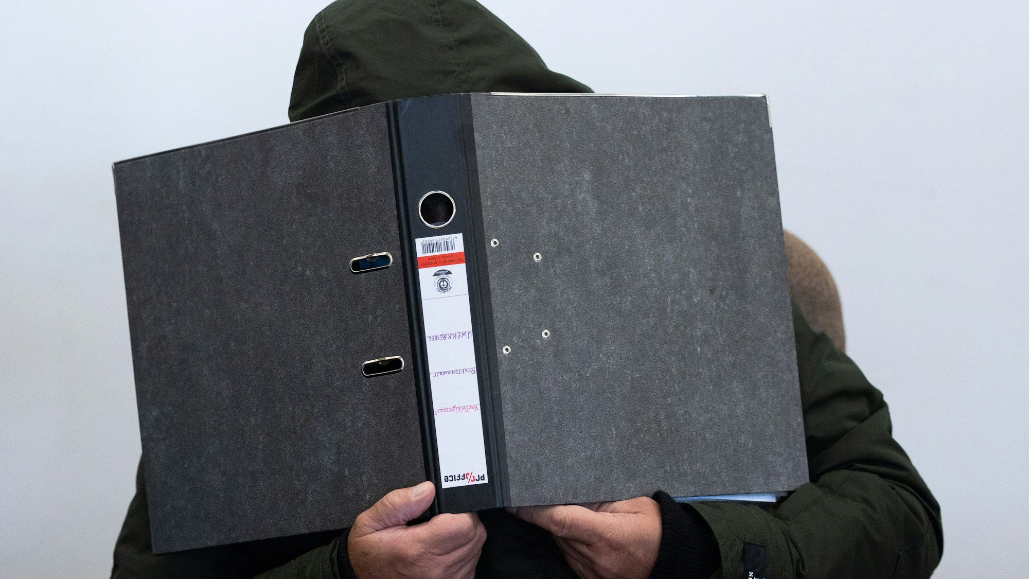 Der Angeklagte verbirgt sein Gesicht hinter einem Aktenordner.