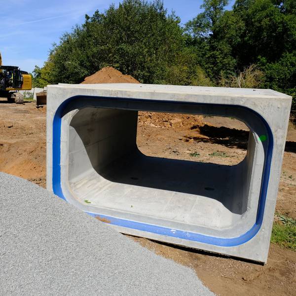 An einer Baustelle in Satzvey liegt ein kastenförmiges Betonrohr, das zum Hochwasserschutz eingesetzt wird. Im Hintergrund sind ein Bagger und ein Lkw zu sehen.