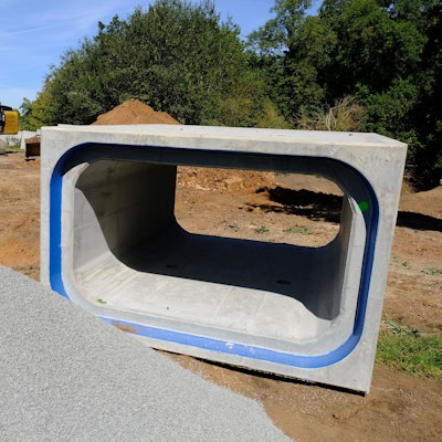 An einer Baustelle in Satzvey liegt ein kastenförmiges Betonrohr, das zum Hochwasserschutz eingesetzt wird. Im Hintergrund sind ein Bagger und ein Lkw zu sehen.