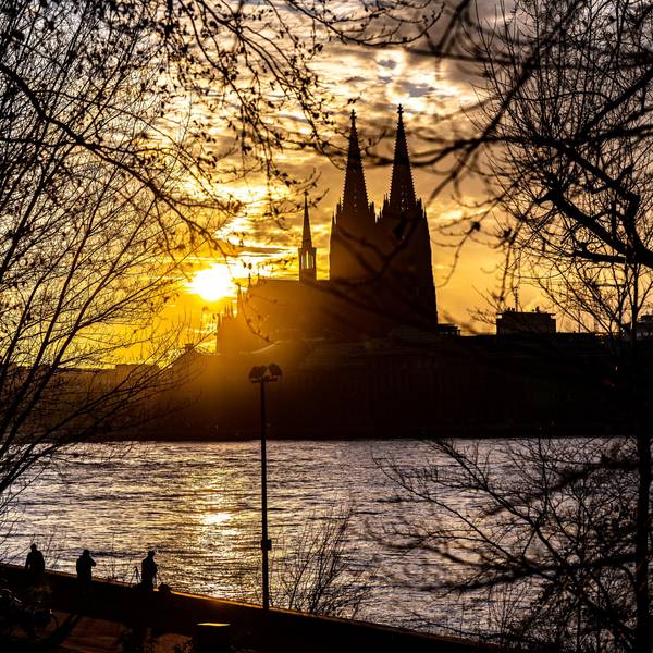 Die Silhouette des Kölner Doms ist im Sonnenuntergang von der gegenüberliegenden Seite des Rheins zu sehen.
